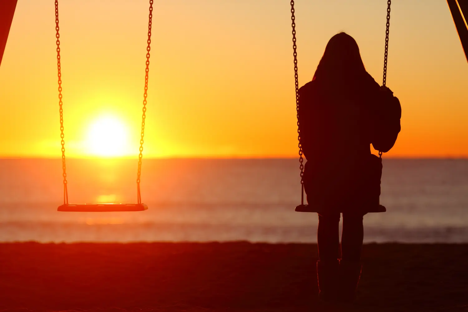 Alleinstehende Frau auf einer Schaukel sitzend und den Sonnenuntergang betrachtend